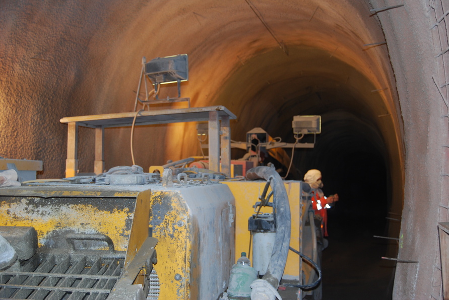 Innenansicht des Fluchtstollens im Schürzebergtunnel mit Spritzbetonmaschine, Tunnelausbau in Stahlfaserspritzbeton und Beleuchtung zur Sicherheit