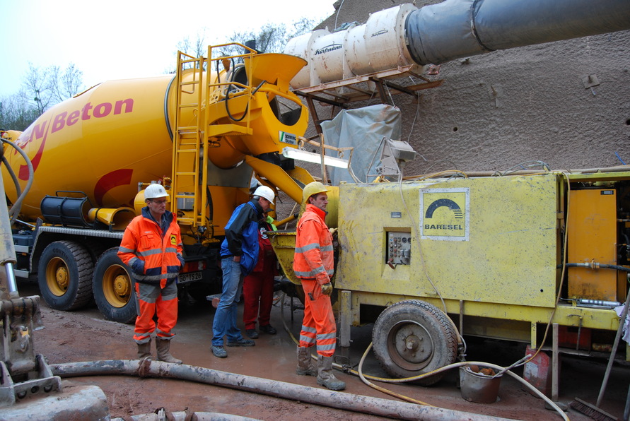 Stahlfaserbeton wird am Schürzebergtunnel über Förderanlage von Baresel eingebracht, Arbeiter überwachen den Materialfluss vom Mischfahrzeug zur Spritzbetonmaschine